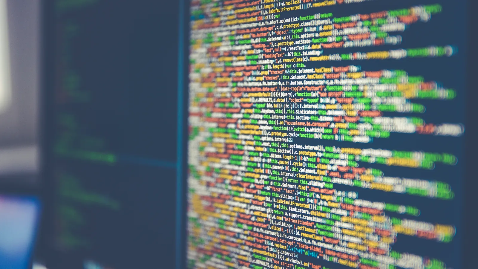 Lines of colorful source code on a dark computer monitor, shown at an angle with shallow focus.