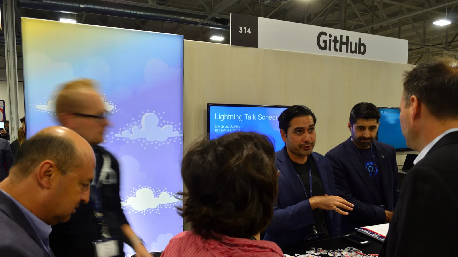 Developers gathered at the GitHub booth at a technology summit, talking in front of the stand.
