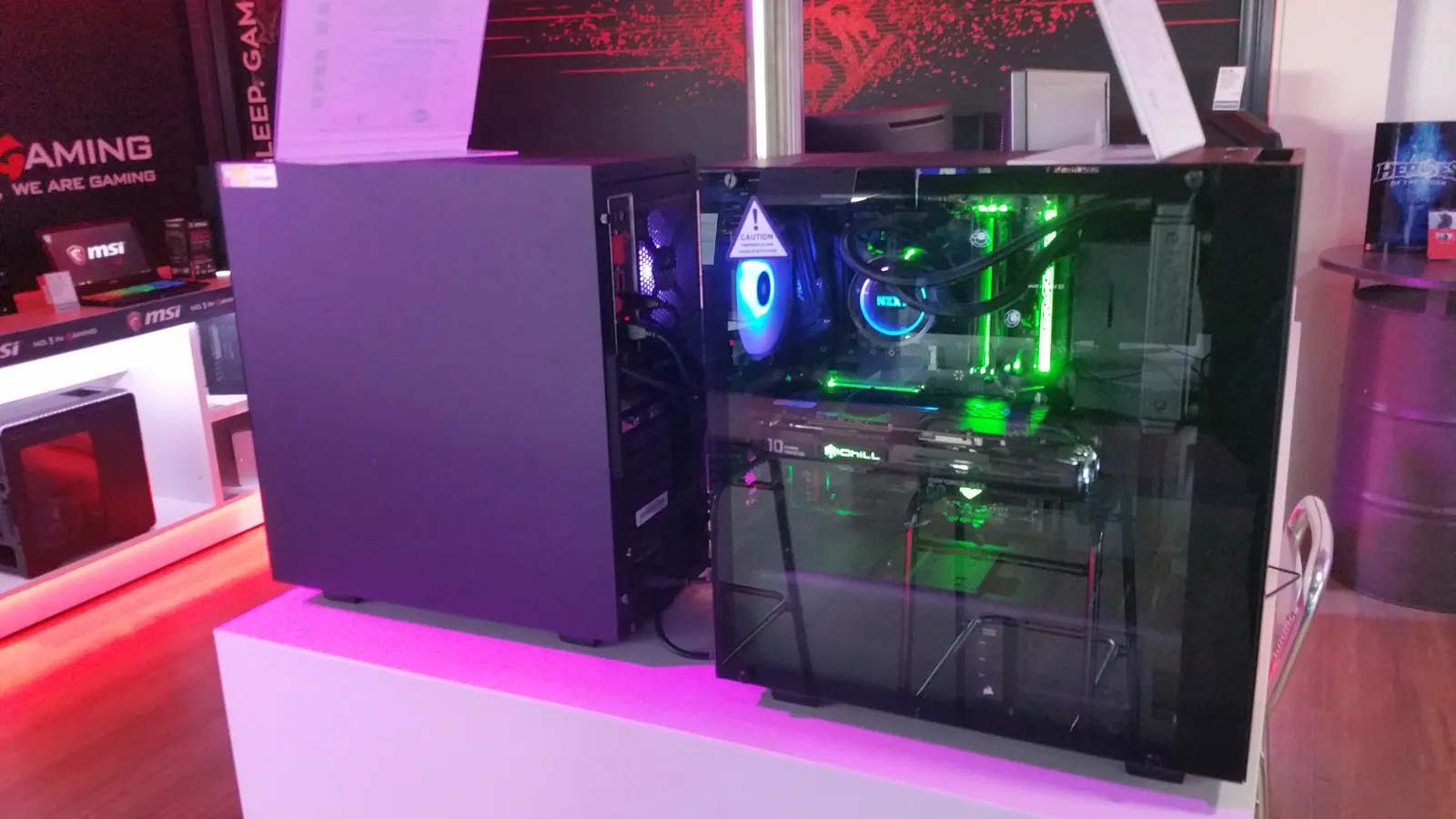 A gaming PC with a glass side panel and green and blue RGB lighting on a store display