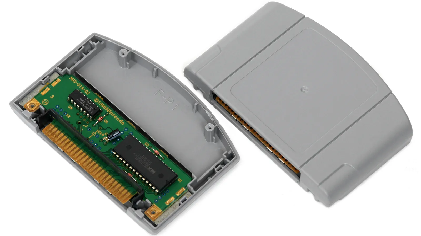 An opened Nintendo 64 game cartridge with its circuit board and ROM chip exposed beside the grey shell