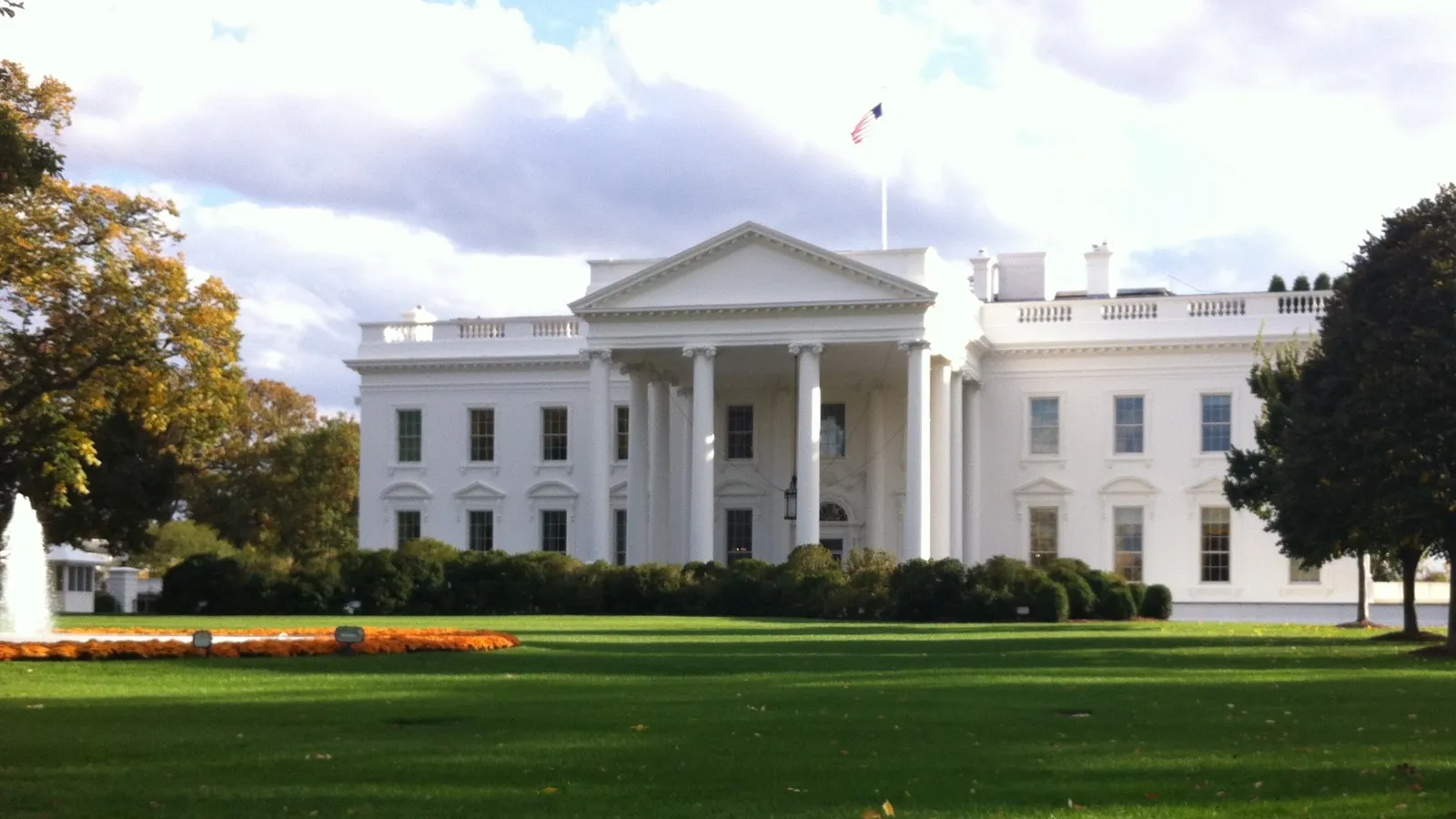 The north facade of the White House at 1600 Pennsylvania Avenue behind a green lawn.